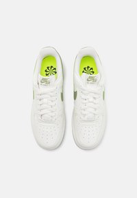 Paire de baskets blanches Nike Air Force 1 avec un swoosh vert et des semelles intérieures vert vif présentant un motif floral noir, vues de dessus.