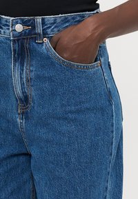Džíny s vysokým pasem v modré denimové barvě, které mají klasický pět pocket design, kontrastní švy a hladkou texturu, vhodné pro každodenní nošení.