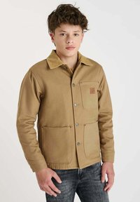 Bruine canvas jas met een corduroy kraag, voorzien van een borstzak en twee voorzakken, bevestigd met drukknoopsluitingen. Casual ontwerp.