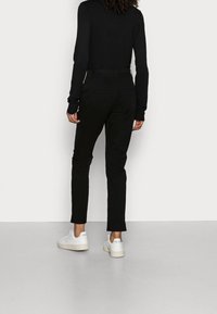 Černé kalhoty s úzkým střihem, vyrobené z hladké látky. Nošeny s tričkem s dlouhým rukávem a bílými teniskami. Minimalistický design, bez viditelných vzorů.