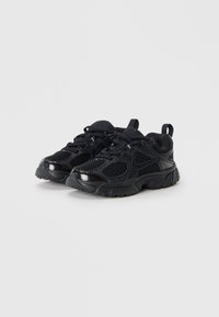 Chaussures de sport noires avec une tige en mesh et des accents brillants, présentant un bout arrondi, une semelle rembourrée et une languette arrière pour un enfilage facile.