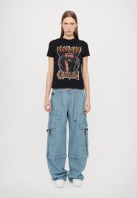 Μαύρη βαμβακερή T-shirt με γραφικό σχέδιο ενός τίγρη και κείμενο. Μπλε τζην cargo παντελόνι με τσέπες και μεταλλικές λεπτομέρειες. Λευκά αθλητικά παπούτσια.