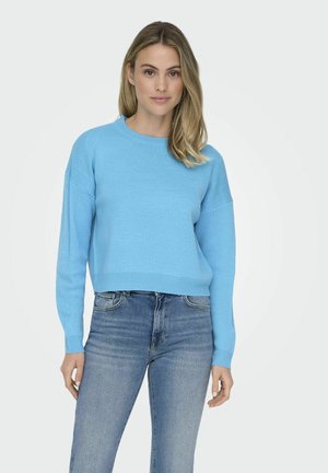 Pull en tricot bleu clair à manches longues et encolure ronde, doté d'un ourlet et de poignets côtelés, porté sur un jeans en denim.
