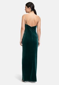 Zielona aksamitna sukienka maxi z głębokim dekoltem na plecach, cienkimi regulowanymi ramiączkami oraz dopasowaną sylwetką, z zapięciem na zamek błyskawiczny z tyłu.