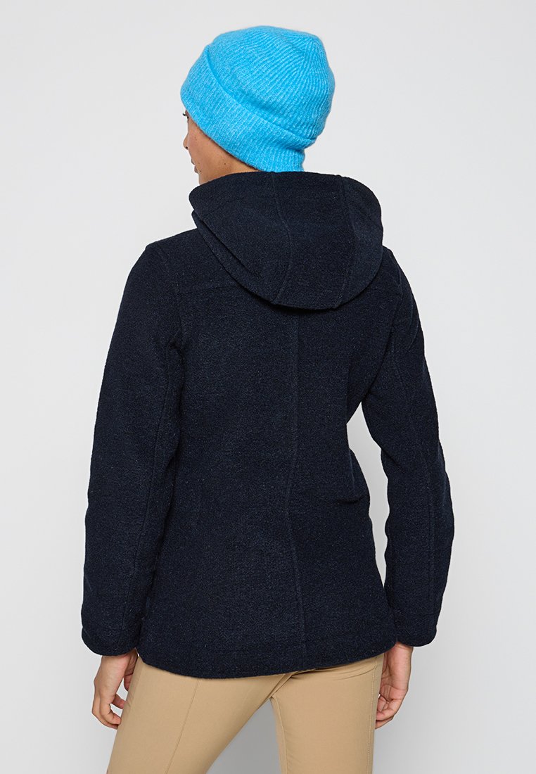 Marineblaue Fleecejacke mit Kapuze, die eine strukturierte Oberfläche und lange Ärmel hat. Getragen mit einer leuchtend blauen gestrickten Mütze.