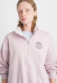 Felpa rosa chiaro con colletto a mezza zip, caratterizzata da un logo ricamato nero "PARIGI" e una grafica a tema sportivo. Tessuto morbido.