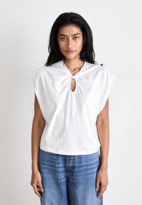 White cotton top featuring a keyhole design, wide sleeves, and a relaxed fit, paired with blue jeans for a casual look.
