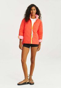 Pohodlná prošívaná bunda v jasně korálové barvě s růžovou podšívkou. Obsahuje přední zip, stahovací detaily a kontrastní manžety na rukávech.