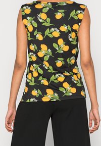 Svart ärmlös topp med ett mönster av citroner och blommor, med gröna blad och vita blommor. Tillverkad av lättviktig tyg; figursydd stil.