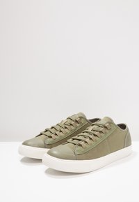 Baskets vert olive en toile et matière synthétique, dotées d'un bout lisse, de lacets contrastants et d'une semelle en caoutchouc blanche.