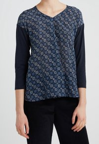 T-paita tummansinisellä värillä, jossa on kukkakuosiset etupuoli ja tasapaksut hihat. V-kaula-aukko ja löysä istuvuus. Pehmeä kangas, jossa on teksturoitu ilme.