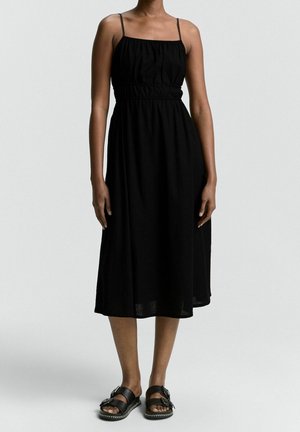 Czarna sukienka bez rękawów z marszczoną górą i rozkloszowanym dołem, wykonana z lekkiego materiału. Do tego czarne sandały wsuwane z klamrami.
