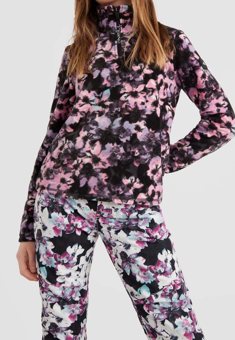 Femme portant un pull en polaire à motifs floraux rose, noir et violet avec une fermeture éclair et un pantalon assorti à motifs floraux.