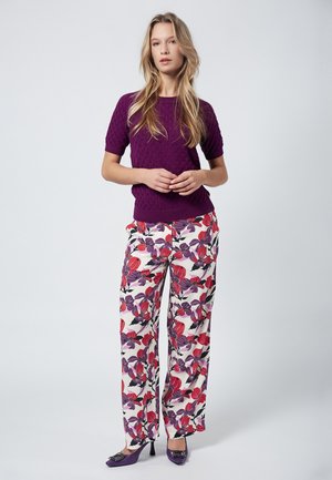 Purple knit top with a textured pattern, paired with white pants featuring large red and purple floral designs. Model wearing purple heels.