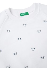Felpa bianca con colletto a coste e accenti a forma di cuore argentato sparsi sul davanti. Etichetta con la scritta "United Colors of Benetton."