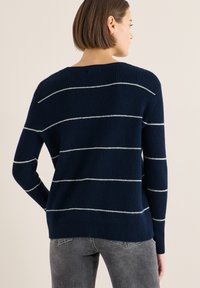 Pull en maille bleu marine avec des rayures blanches, doté d'une coupe décontractée et d'une texture côtelée. Détails de coutures visibles au niveau de l'encolure et des ourlets.