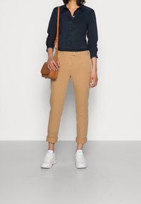 Navy button-up shirt, beige chinos, and white sneakers. Brown crossbody bag. Chinos rolled at cuffs, shirt smooth with small collar.