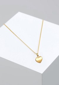 Collar de tono dorado con un colgante en forma de corazón liso y pulido. La cadena es fina y delicada, resaltando la forma y el color del colgante.