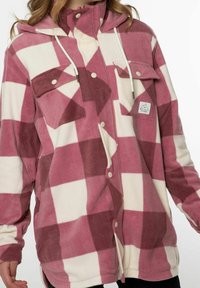 Giacca di flanella a quadri rosa e crema con cappuccio, bottoni a scatto e tasche sul petto; texture morbida e design caldo.