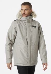 Lichtgrijze geïsoleerde jas met een met bont gevoerde capuchon. Heeft zwarte accenten en een logo op de borst, twee voorzakken en een ritsluiting.