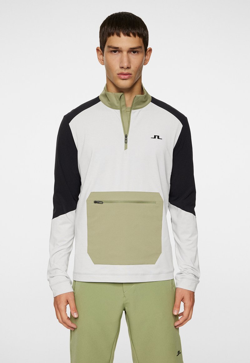 Quarter-zip trøje i hvid, sort og olivengrøn. Har en stor forlommes og et logo på brystet. Glat stofstruktur.