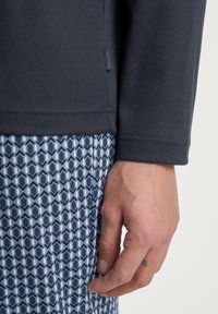 Haut gris à manches longues avec un détail de couture, associé à un pantalon bleu à motifs présentant des designs géométriques dans des tons de bleu clair et bleu foncé.