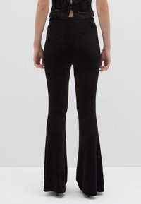 Pantaloni neri a campana in un tessuto morbido ed elastico, con una texture liscia, caratterizzati da una vita aderente e un allargamento graduale dal ginocchio.