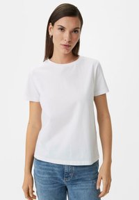 White cotton t-shirt, short sleeves, round neckline, subtly embossed logo on the chest, paired with blue denim jeans.