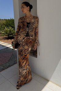 Brown tiger print silk jacket and matching long skirt with a black top underneath. Accessories include layered necklaces and a small bag.