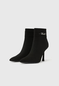 Melnas augstpapēžu potīšu zābaki ar smailiem purngaliem, ribotiem aprocēm un sudraba logotipa detaļu ārējā pusē.