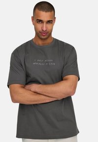 Gray cotton t-shirt with short sleeves, featuring white text "I ONLY ACCEPT APOLOGIES IN CASH" across the chest. Simple, relaxed fit design.