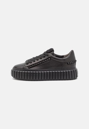 Czarny skórzany sneaker na platformie z grubą żeberkowaną podeszwą, czarnymi sznurówkami i dekoracyjnymi czarnymi ćwiekami po bokach i na pięcie.