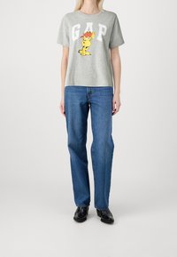 Camiseta de algodón gris con el logo "GAP" y un personaje de dibujos animados, combinada con jeans de pierna recta azules y zapatos negros.