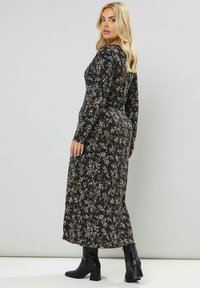 Abito nero a maniche lunghe con silhouette aderente, design di media lunghezza e sottili motivi floreali nei toni di crema e marrone.