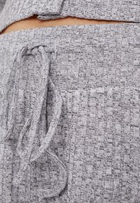 Close-up of gray ribbed knit pants with a tied drawstring waistband and part of a matching top visible above.