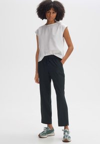 Weißes Kurzarmoberteil, lockere Passform; schwarze Hose mit elastischem Bund; grau-grüne Sportschuhe mit strukturierter Sohle; minimalistisches Design.
