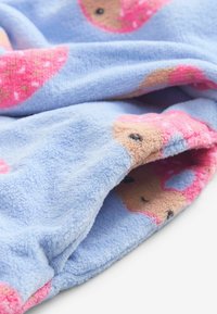 Fleece tæppe i lyseblå med lyserøde og beige donut mønstre. Blød tekstur og let rynket udseende fra at være draperet.