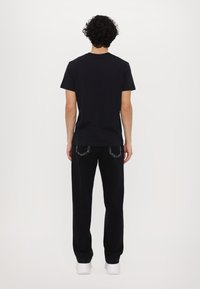 T-shirt de algodão preto com decote redondo combinado com calças de ganga pretas com costuras em contraste, usadas com ténis brancos.