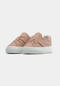 Scarpe slip-on rosa chiaro con un design superiore annodato, suola in gomma bianca e fodera a pois. Texture in tessuto morbido e forma della punta arrotondata.