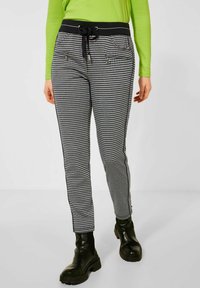 Black and white houndstooth patterned trousers with a black elastic waistband and drawstring, featuring side pockets and slim fit.