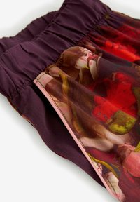 Paarse rok met elastische tailleband. Heeft een kleurrijk bloemmotief in tinten rood en roze. Gladde textuur, contrasterende randen.