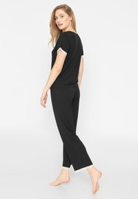 Ensemble de détente noir comprenant un haut à manches courtes avec des détails en dentelle sur les manches et un pantalon avec des accents en dentelle sur l'ourlet. Texture de tissu douce.