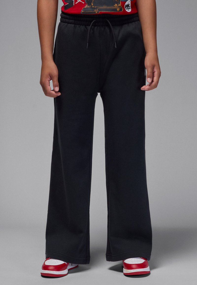 Pantalon de survêtement noir à jambes larges avec une taille élastique et un cordon de serrage. Le tissu est doux et l'ourlet est fini par un subtil revers.