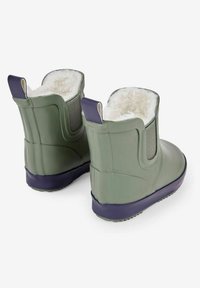Stivali di gomma verdi con suola viola, fodera in pile e pannelli elasticizzati laterali per facilitare l'indossamento. Presenta un design a caviglia bassa.