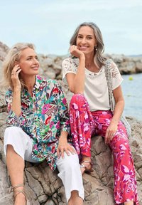 Bloemdrukhemd in opvallende kleuren; witte cropped broek. Metgezel in een witte top, roze met patroon broeken, geaccentueerd met een zilveren tas.