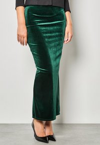 Gonna maxi verde velluto con una texture liscia, design aderente e una leggera lucentezza, abbinata a tacchi a punta neri.