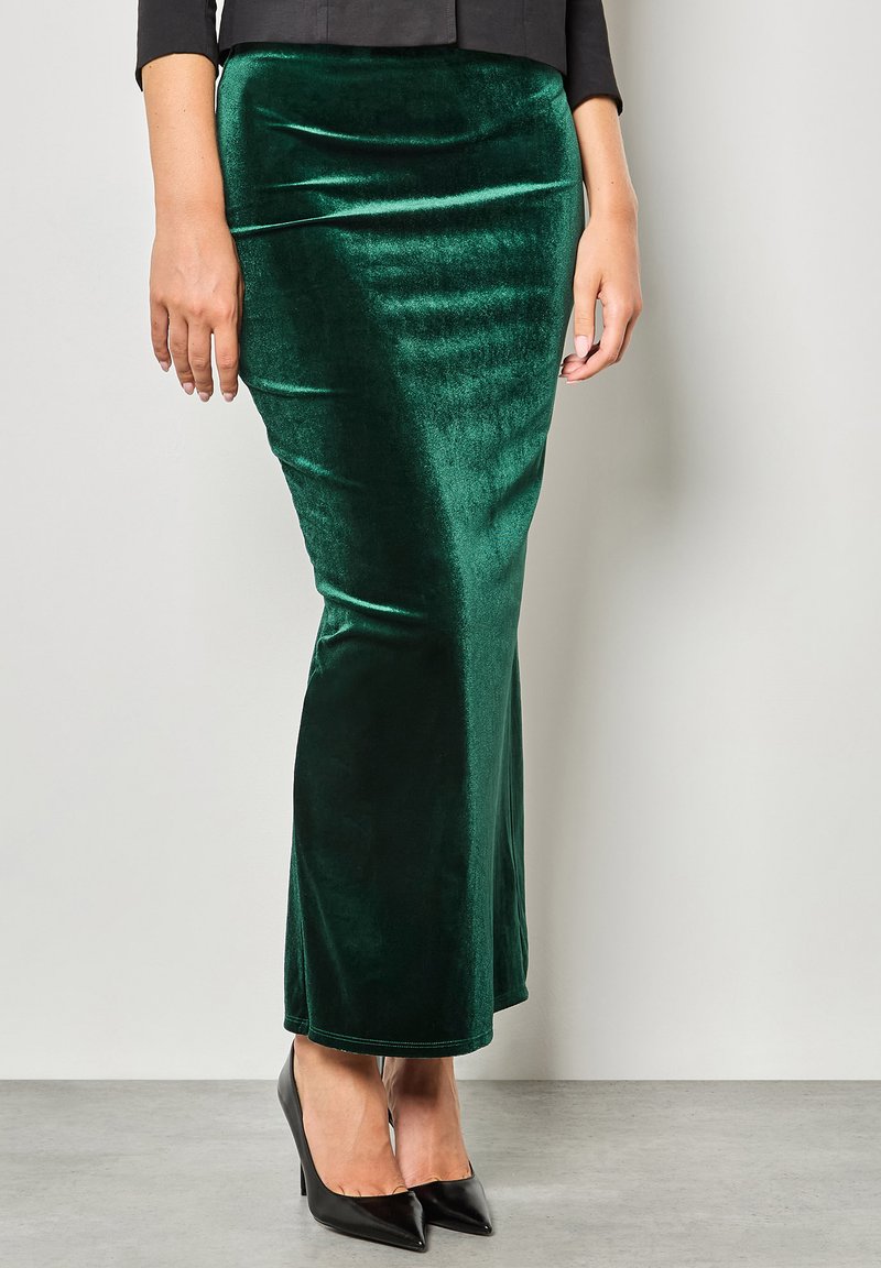 Gonna maxi verde velluto con una texture liscia, design aderente e una leggera lucentezza, abbinata a tacchi a punta neri.