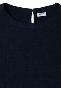 Haut en tissu texturé bleu marine foncé avec un col rond et une petite ouverture fendue dans le dos avec une étiquette en tissu blanche.