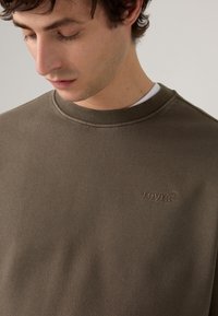 Sudadera verde oliva oscura hecha de una mezcla de algodón. Presenta un cuello redondo y un sutil logotipo bordado de Levi's en el pecho.