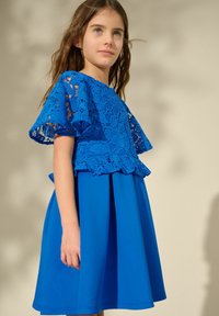 Blauwe jurk met een kanten bovenkant, korte uitlopende mouwen en een geplooide rok. De jurk heeft een uniforme kleur en een getailleerde taille.